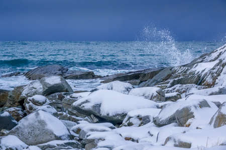 Winter Norway. Snow-covered rocky shore of the ocean. Water spray of the surf waveの写真素材