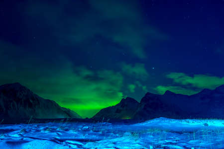 Norway. Lofoten. Winter night. Snow-covered grass and mountains. Clouds in the sky and northern lightsの写真素材