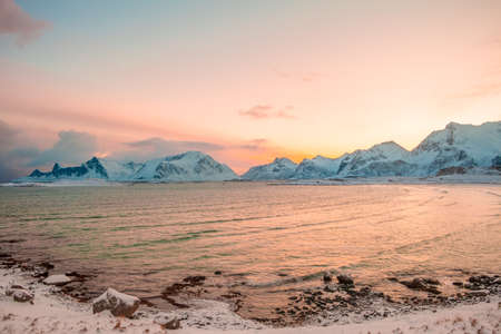 Winter. Norwegian fjord surrounded by snow-capped mountains in the early morning. Pink sky from...