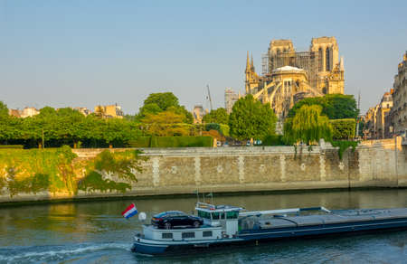 France. Paris. Sunny summer morning on the Seine embankment. Notre Dame in scaffolding after a fire in 2019. Barge on the riverの写真素材