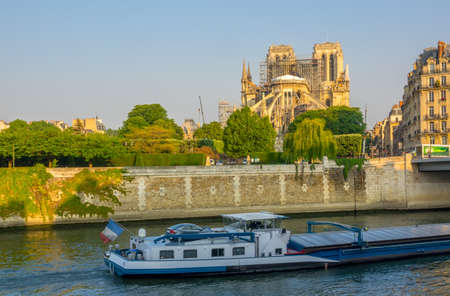France. Paris. Sunny summer morning on the Seine embankment. View of Notre Dame in scaffolding after a fire in 2019. Barge on the riverの写真素材