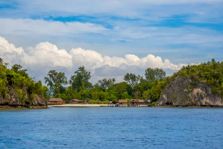 Island in indonesia. Raja Ampat. Several traditional huts on the shore between the rocks and the beachの写真素材