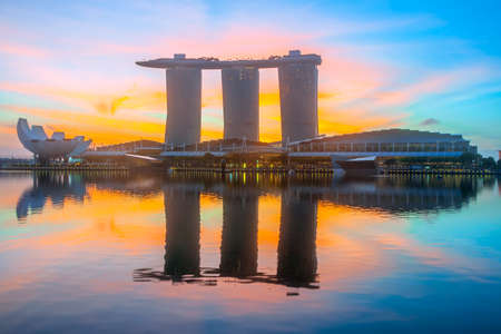 Morning in Singapore. Three buildings of the hotel in the form of a ship are reflected in the calm water of Marina Bay. The rising sun painted the sky in orange and redのeditorial素材