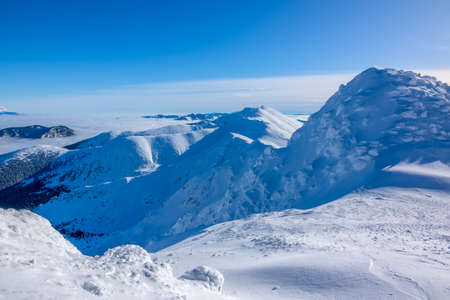 A lot of snow on the peaks and slopes of the winter mountains. Sunny weather and cloudless blue sky