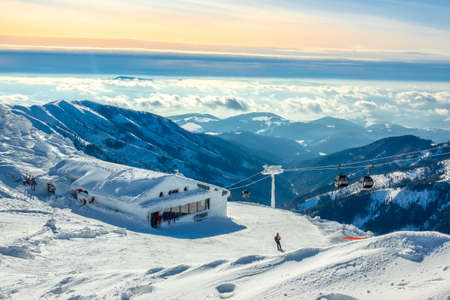 Winter mountains. Snow-capped peaks and fog in the valleys. Blue and pink sky over the ski run. Ski lift and barの写真素材