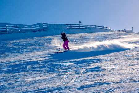 Sunny day on a snowy ski slope. Unrecognizable girl skier raises snow dustの写真素材