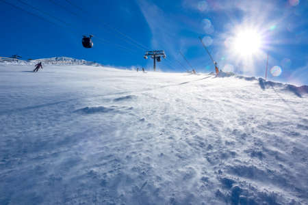 Sunny weather at the ski resort. A strong wind drives snow on the ski slope. Ski lift in the backgroundの写真素材