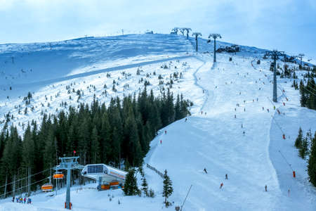 Skiers on the ski slope. Two lines of a ski lift. The sun barely breaks through the cloudsの写真素材