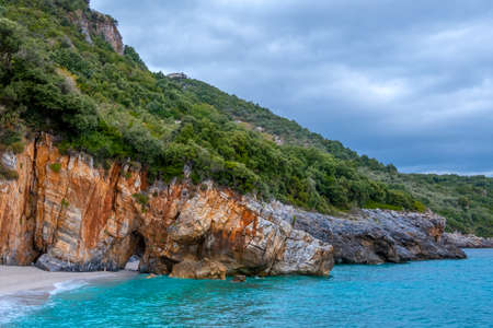 Rocky forest shore of the sea in cloudy weather. Villa on the slope. There is a natural stone arch on the beachの写真素材