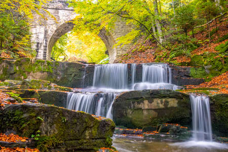 Sunny day in the summer forest. Arch of an old stone bridge. Small river and several natural waterfallsの写真素材