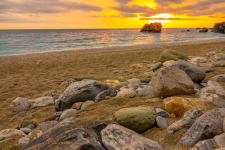 Colorful sunset over the calm sea. Coarse sand beach with stonesの写真素材