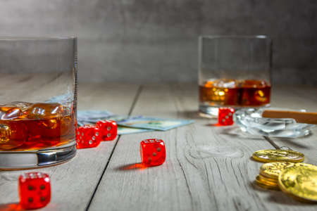 Rustic wooden table. Two glasses of whiskey with ice cubes and a cigar in an ashtray. Dollar bills and dice. A few bitcoin coinsの写真素材