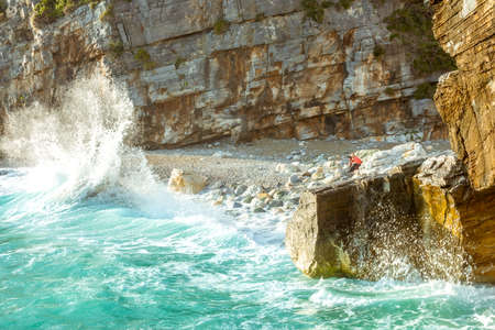 Spray surf on a rocky shore. Girl photographer on a wild beachの写真素材