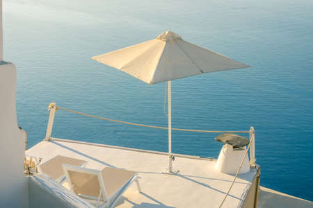 Greece. A quiet summer evening in Santorini. Two sun loungers and an umbrella on the balcony with a sea viewの写真素材
