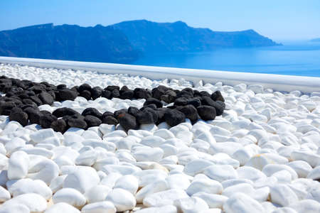 Greece. Thira island. Sunny day in Santorini. Black and white stones on the terrace with sea viewの写真素材