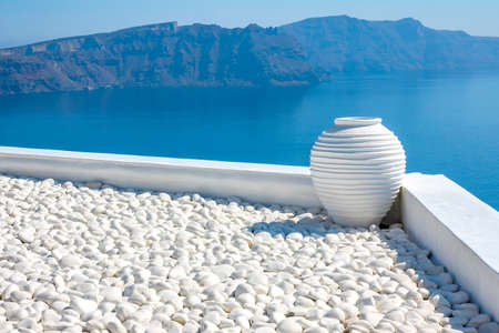 Greece. Sunny day on Santorini. White pebbles and white stone vase. Seascape with rocky islandsの写真素材