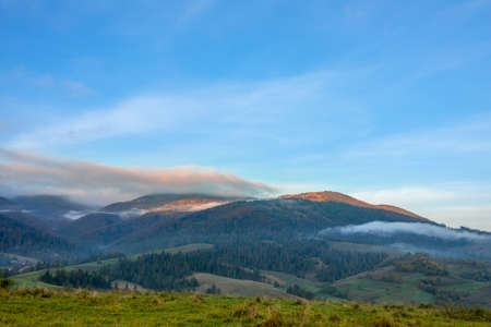 Blue sky over wooded hills. Morning fog and rays of sunlight over the peaks