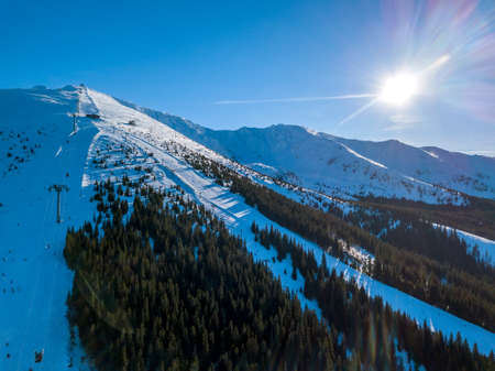 Slovakia. Jasna in sunny winter weather. Ski slopes in the wooded mountains. The sun shines brightly in the blue sky. Aerial viewの写真素材
