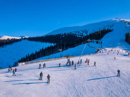 Slovakia. Winter Jasna in sunny day. Ski slopes in the wooded mountains. Sun shines brightly and blue sky. Aerial viewのeditorial素材
