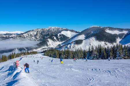 Winter mountains. Wide and gentle ski slope in sunny weather. Lots of skiers. Light fog in the valleyの写真素材