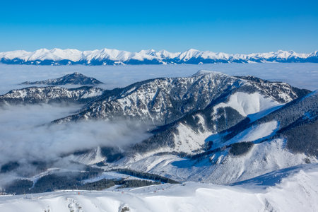 The tops of winter mountains and mist in the valleys in a ski resort. Sunny weather and blue sky. Aerial viewの写真素材