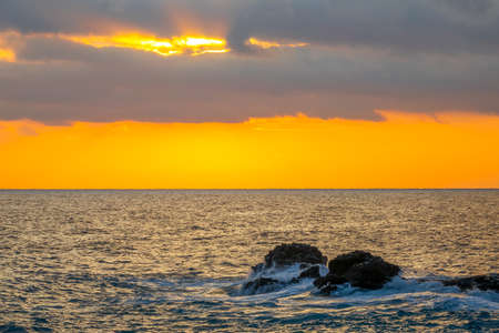 Amazing sunset colors in cloudy skies. Coastal stones in the calm seaの写真素材
