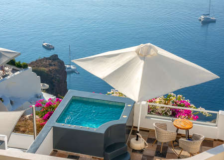 Santorini. Terraces on the high shore of Thera Island. Swimming pool and loungers for relaxing in sunny weather. Yachts by the shoreのeditorial素材