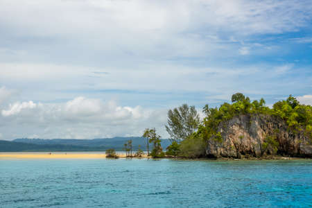 An Indonesian island in the Raja Ampat archipelago. Sand spit on the coast of a tropical island. A few unrecognizable people. Lonely hut hides behind treesの写真素材