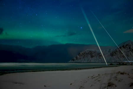 Winter Norway. Night beach between the mountains in Lofoten. Light northern lights and people with flashlightsの写真素材