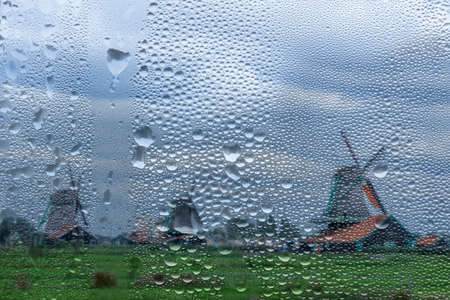 Netherlands. Old windmills in the Zaanse Schans in rainy weather. View through a window with raindropsの写真素材