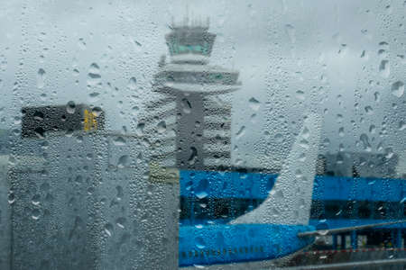 Rainy weather in a modern airport. Parked plane. View through a window with raindropsの写真素材