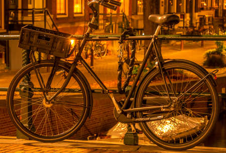 Netherlands. Night Amsterdam. Bicycle with a luggage basket is parked at the canal fence and secured with an anti-theft chainの写真素材