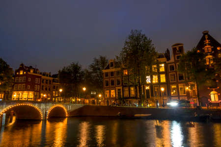 Netherlands. Night on the Amsterdam canal. Old stone bridge and typical houses on the embankment. Traffic on the water and streetsの写真素材