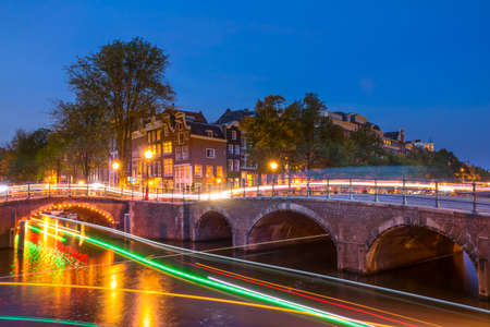 Netherlands. Late summer evening on a canal in Amsterdam. Lots of trails from boat and car lightsの写真素材