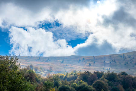Summer Ukrainian Carpathians. Clouds in the sky and sunlight illuminating a hillside with haystacksの写真素材