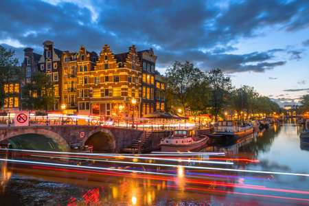 Netherlands. Typical Dutch houses on the evening embankment of Amsterdam. Houseboats are moored off the coast. Light trails from the front and rear lights of cars and boatsの写真素材