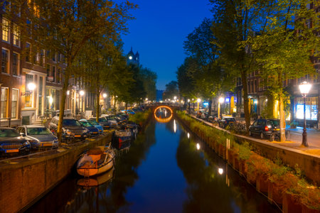Netherlands. Summer night in Amsterdam. Lanterns and parked cars on the embankments. Boats are moored along the banks of the canalの写真素材