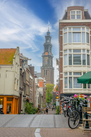 Netherlands. Cloudy summer day in Amsterdam. People and bicycles on a narrow street in downtown with typical houses and the dome of an ancient cathedralの写真素材