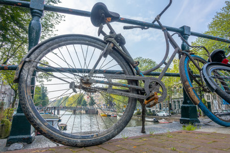 Netherlands. Summer day in Amsterdam. Dirty old bicycle near the canal fenceの写真素材