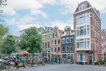 Netherlands. Summer day in Amsterdam. Light clouds in the blue sky. Several bicycles are parked near the railing of a bridge over a canalの写真素材