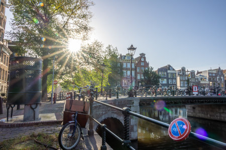 Netherlands. Sunny summer morning in Amsterdam. Traditional houses on the banks of the canal. Many bicycles near the bridge fence.の写真素材