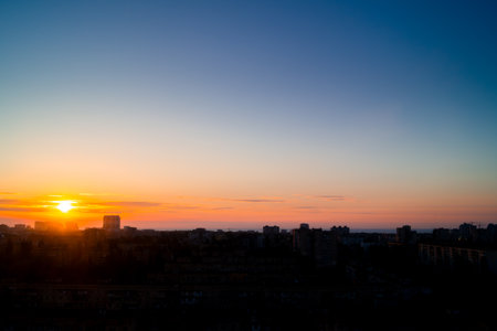 Dawn in a clear summer sky over the city. The rising sun breaks through light clouds on the horizon. Silhouettes of buildings in backlightの写真素材