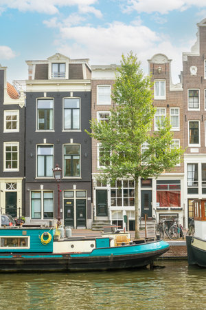 Netherlands. Summer day in Amsterdam. Typical Dutch houses and bicycles on the canal embankment. Parked houseboats - barges on the waterの写真素材