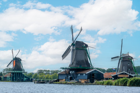 Netherlands. Cloudy summer day in Zaanse Schans. Three vintage but functioning windmills on the bank of a canalの写真素材