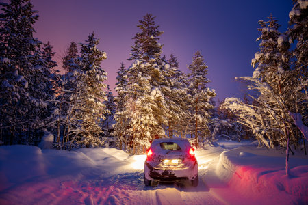 Finnish Lapland in winter. Snow-capped forest at night. Snowy car with headlights on forest roadの写真素材