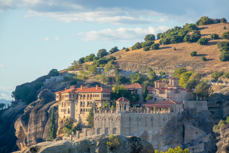 Sunny summer day in northern Greece. Large rock monastery in Meteora near green hill against blue skyの写真素材