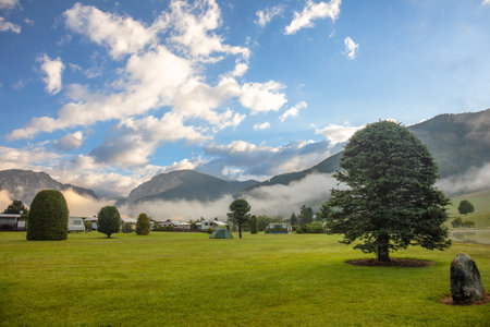 Austria. Campers and tents at a summer campsite in the forested mountains. The rising sun illuminates the clouds and morning fogの写真素材