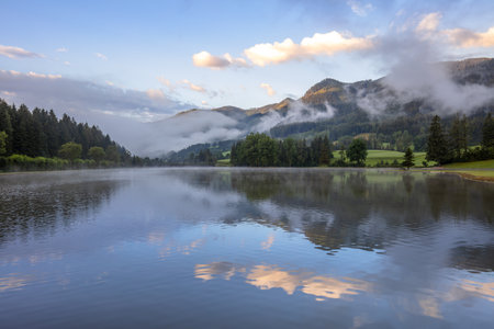 Summer Austria. Forest lake at sunrise. The water mirror reflects the mountains and dawn cloudsの写真素材