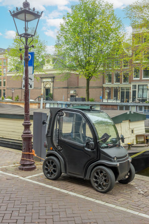 Netherlands. Summer day in Amsterdam. Electric mini-car is tied to a lamppost on the canal embankmentの写真素材