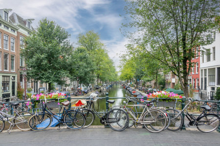 Netherlands. Summer day in Amsterdam. High clouds in the blue sky. Several bicycles are parked near the railing of a bridge over a canalの写真素材
